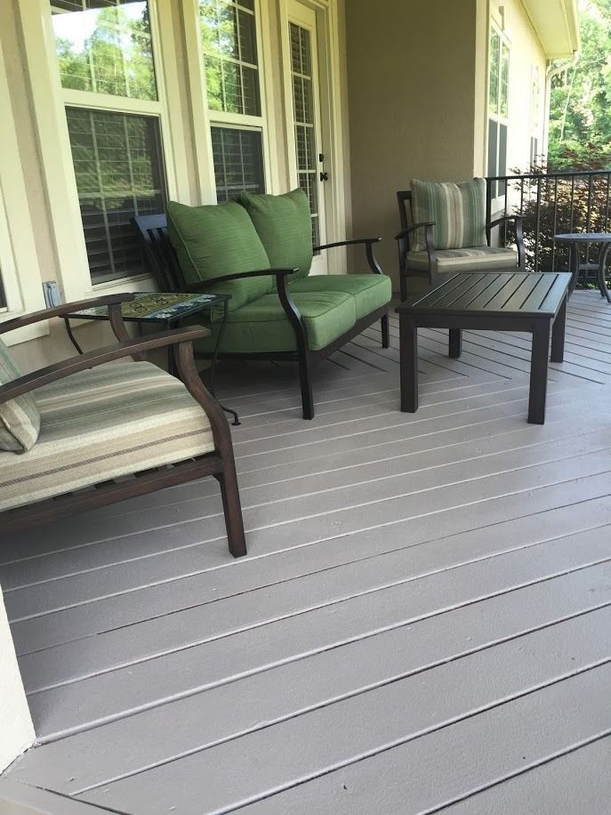 Covered porch with green cushioned chairs and a black coffee table on gray flooring.