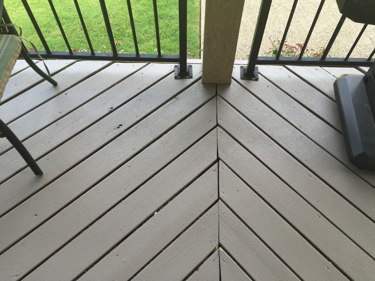 Wooden porch floor with chevron boards, black railing, and a beige support post at the center.
