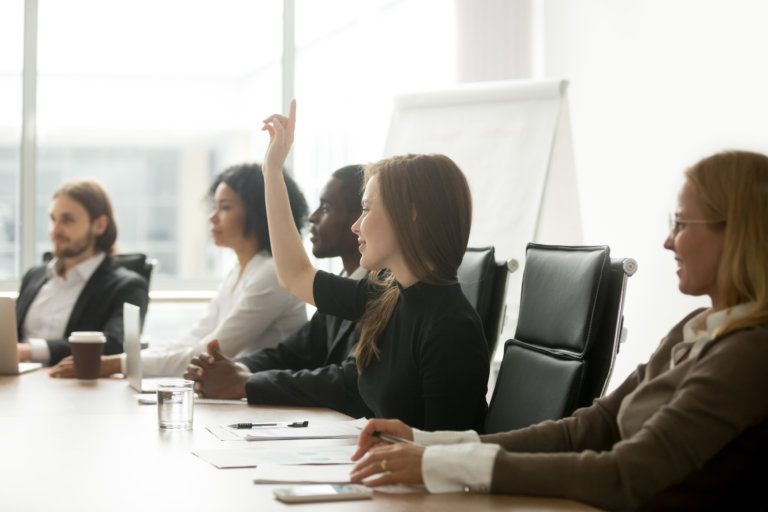 A group of people are sitting at a table with their hands up.