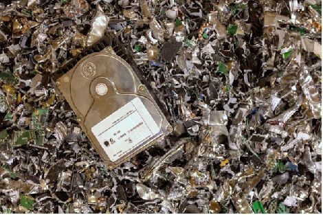 A hard drive is sitting on top of a pile of shredded electronic components.