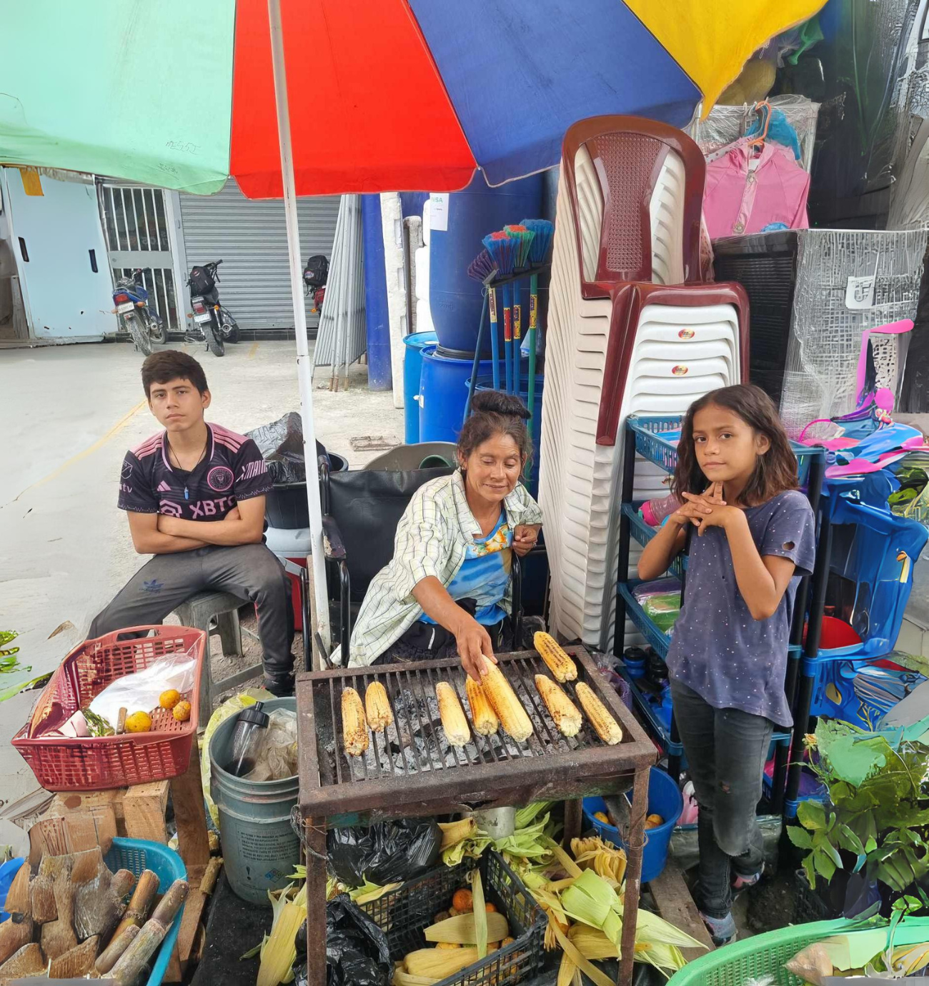 A group of people are sitting under an umbrella eating corn on the cob