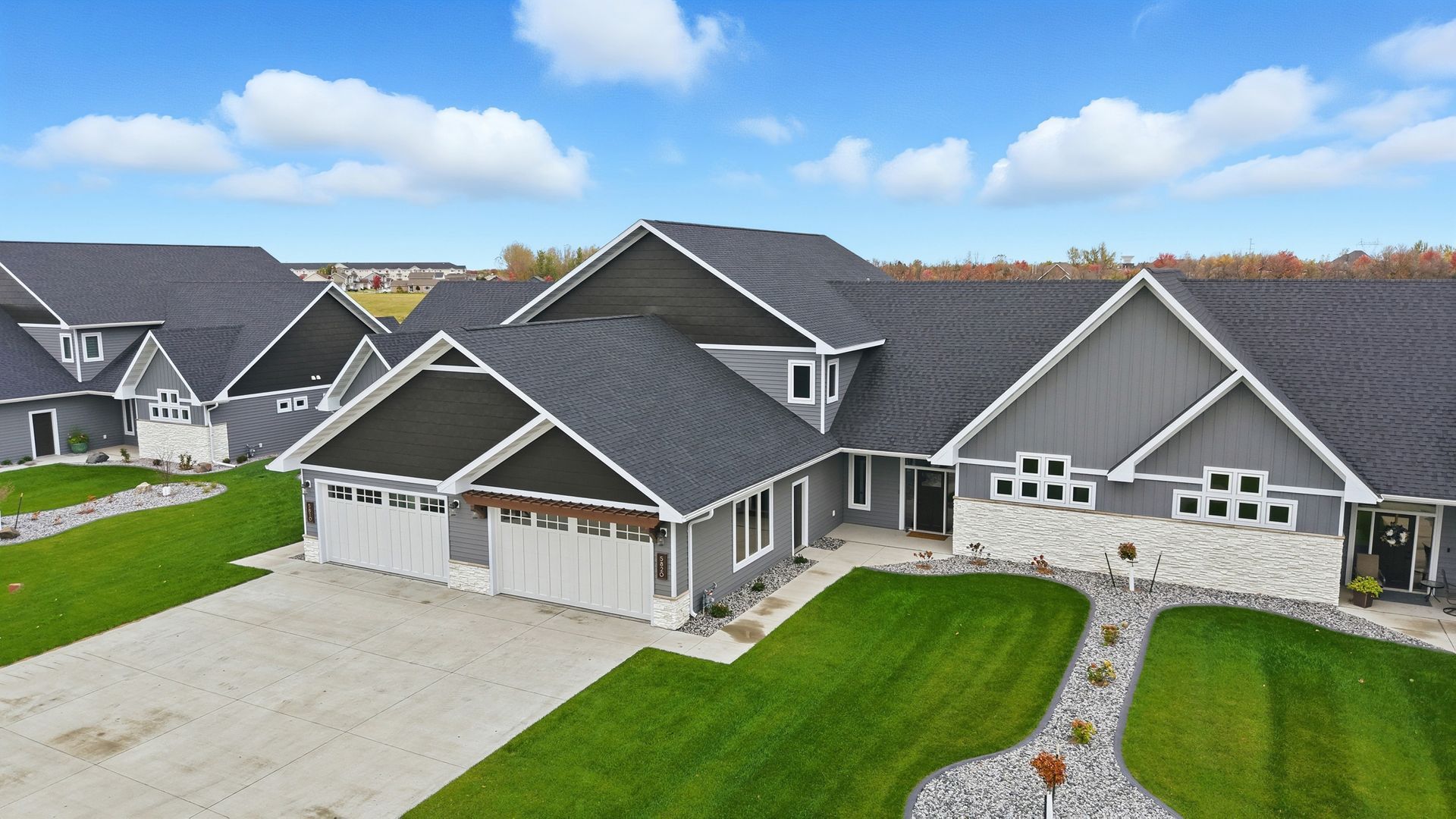 Large gray suburban house with a three-car garage, white trim, and a green lawn under cloudy skies