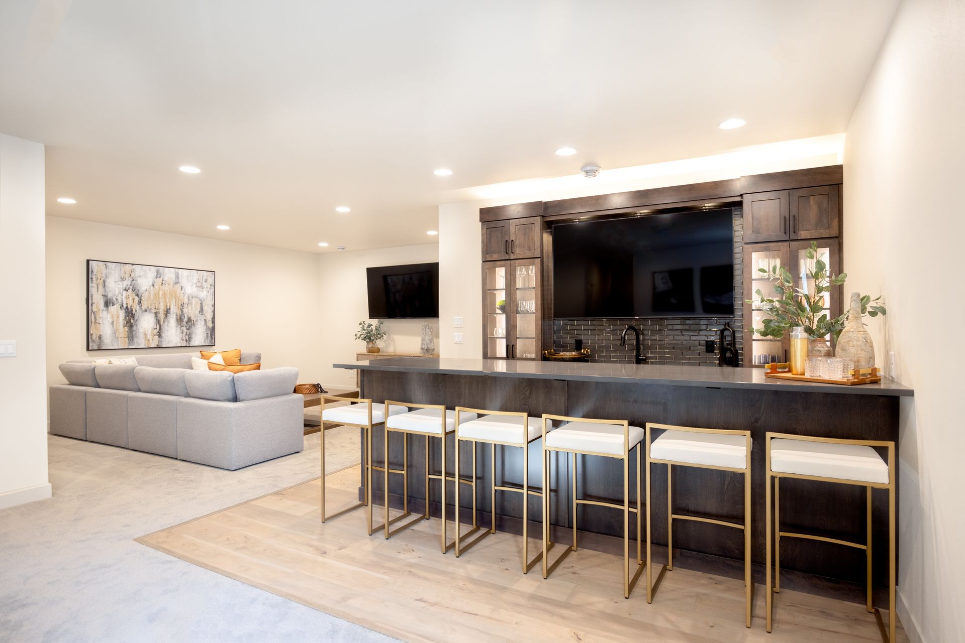 Modern open-plan living room with gray sectional, kitchen island, and bar stools under recessed lighting