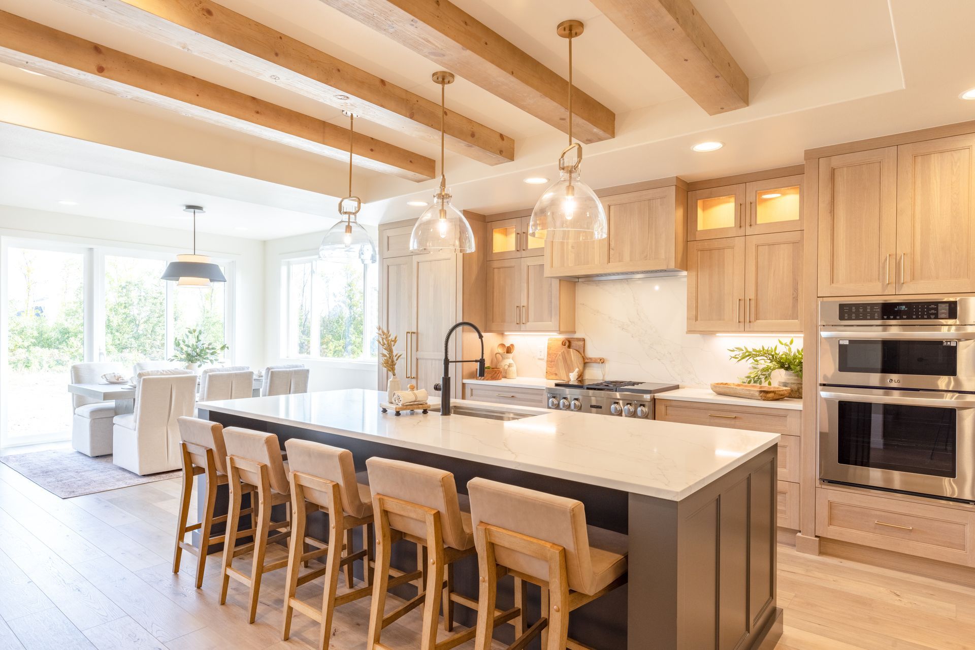 Bright modern kitchen with large island, wooden stools, white cabinetry, and pendant lights.