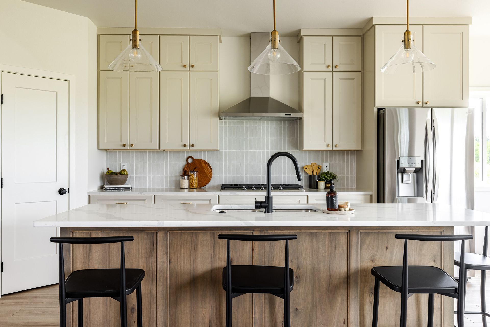 Bright kitchen with white cabinets, marble island, black stools, and stainless steel appliances