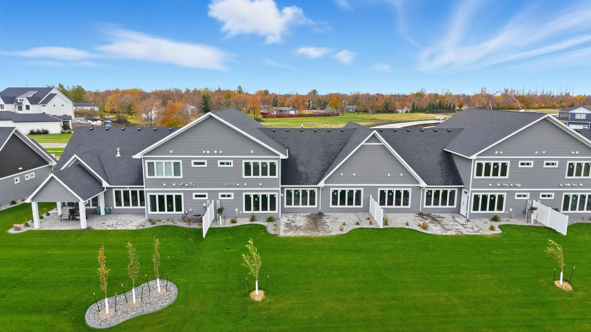 Large gray suburban house with white trim and a wide green lawn under a cloudy sky