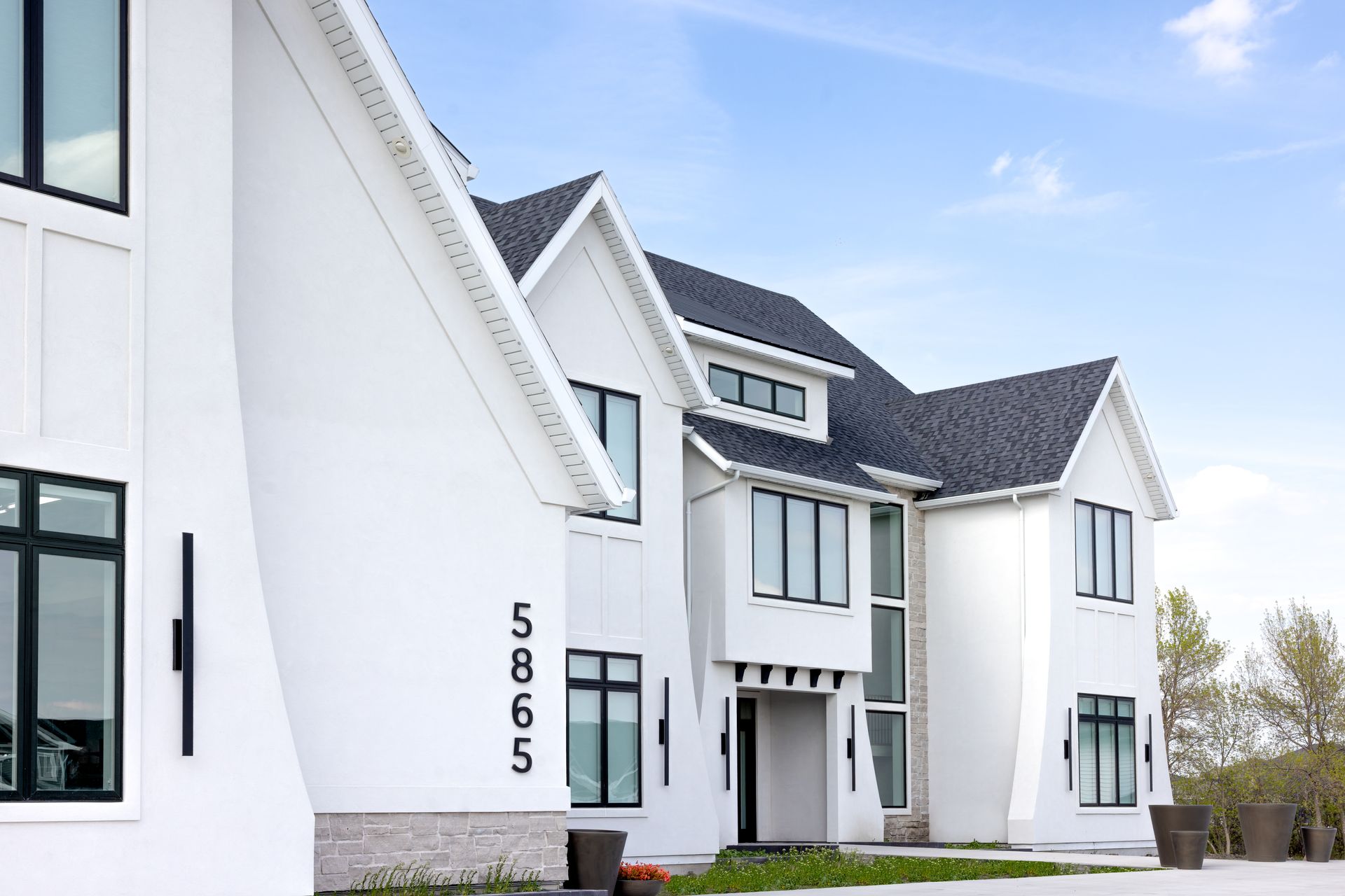 Modern white apartment building with black-trim windows and entryway under a blue sky