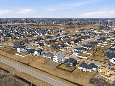 Aerial view of a suburban neighborhood with rows of houses, roads, and open brown fields under a clear sky