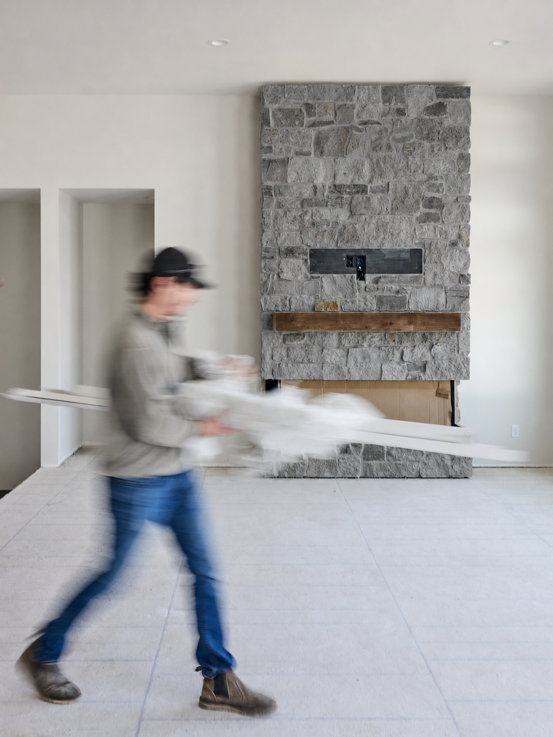 Person walking through a bright room with a stone fireplace and a white sheet-covered couch.