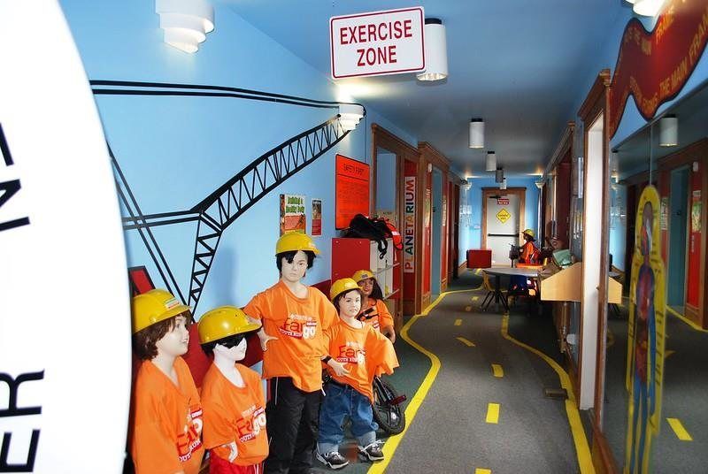 Children's Museum at Yunker Farm Four children in orange shirts and yellow hard hats stand in a hallway painted with a construction crane theme.