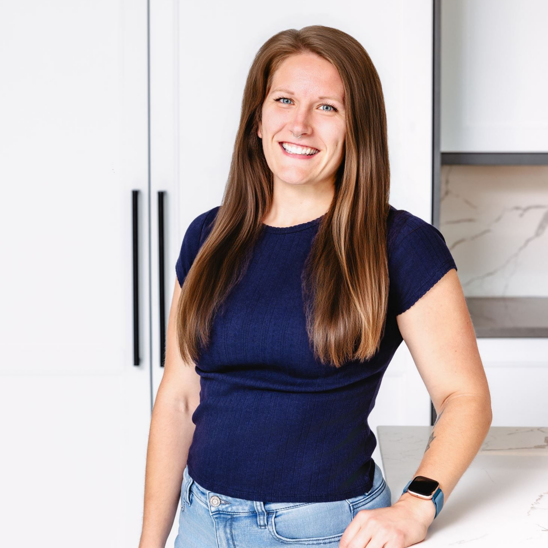 Smiling woman in a navy shirt and jeans standing in a bright kitchen