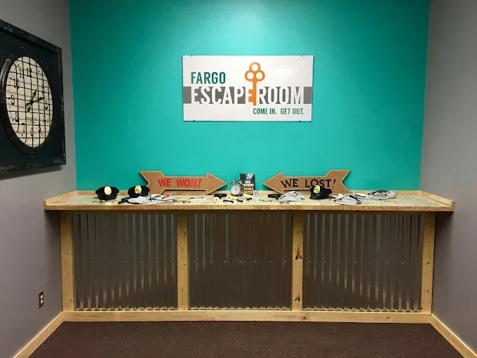Escape House Fargo A teal-walled room with a Fargo Escape Room sign, a large clock, and a counter with