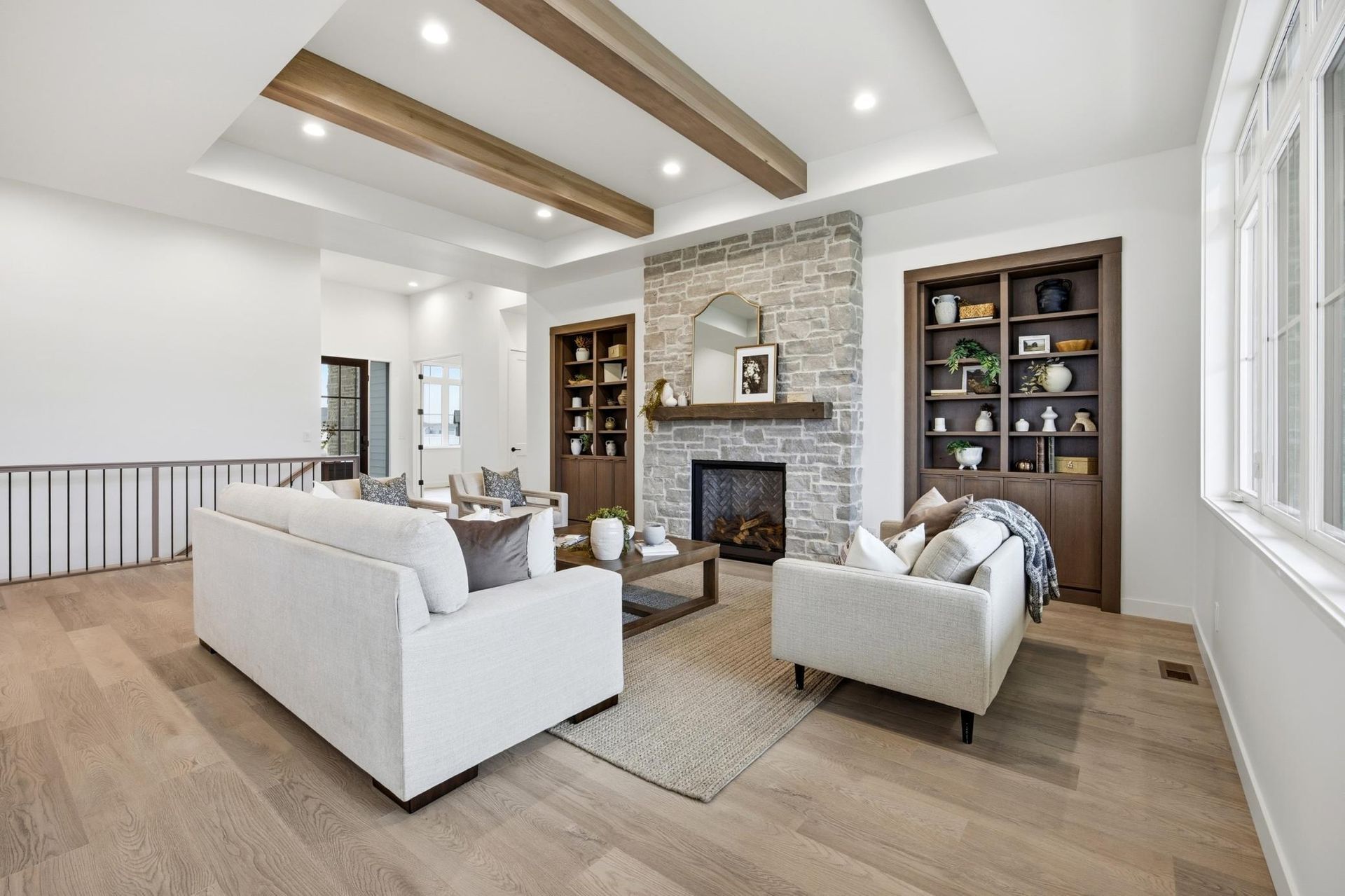 Living room with a stone fireplace, built-in shelves, light-colored sofas, and wood-beam ceiling.
