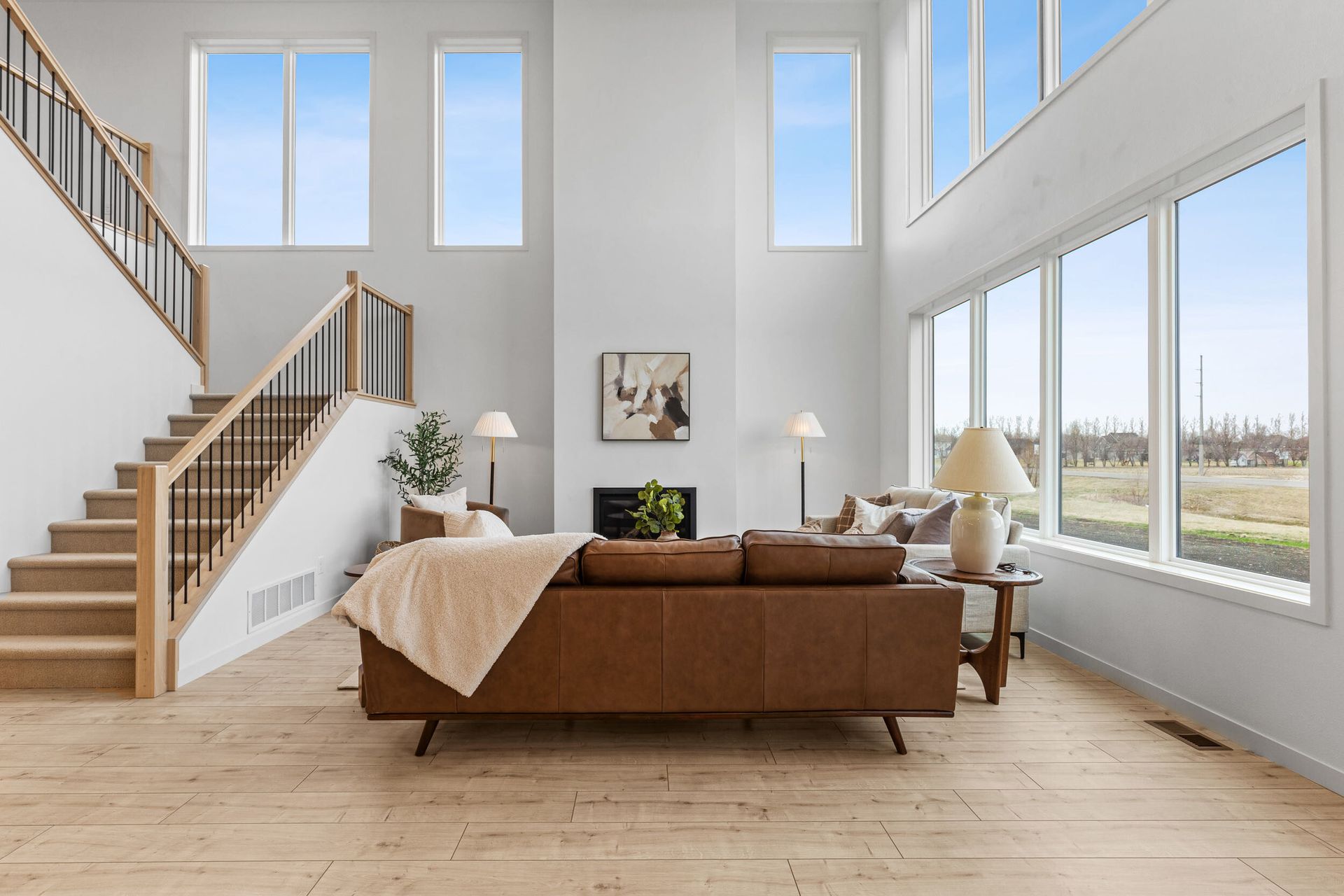 Bright modern living room with brown sofa, staircase, large windows, and natural light