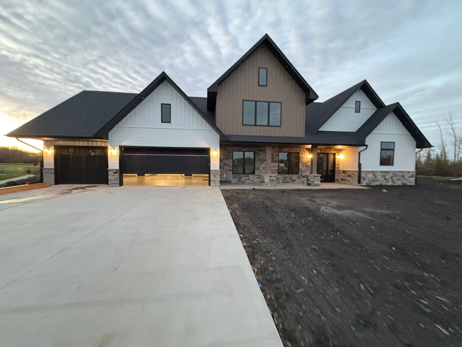 Modern farmhouse-style house exterior at dusk with lit garage and large concrete driveway
