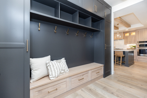 Dark cabinetry frames a light wood bench, drawers, hooks and open cubbies in the mudroom. 