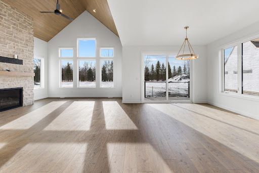 Bright empty living room with vaulted ceiling, fireplace, large windows, and snowy outdoor view