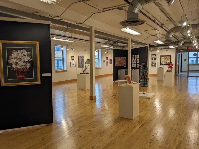 Plains Art Museum An art gallery with hardwood floors, white pedestals, and various framed artworks displayed on walls and stands.