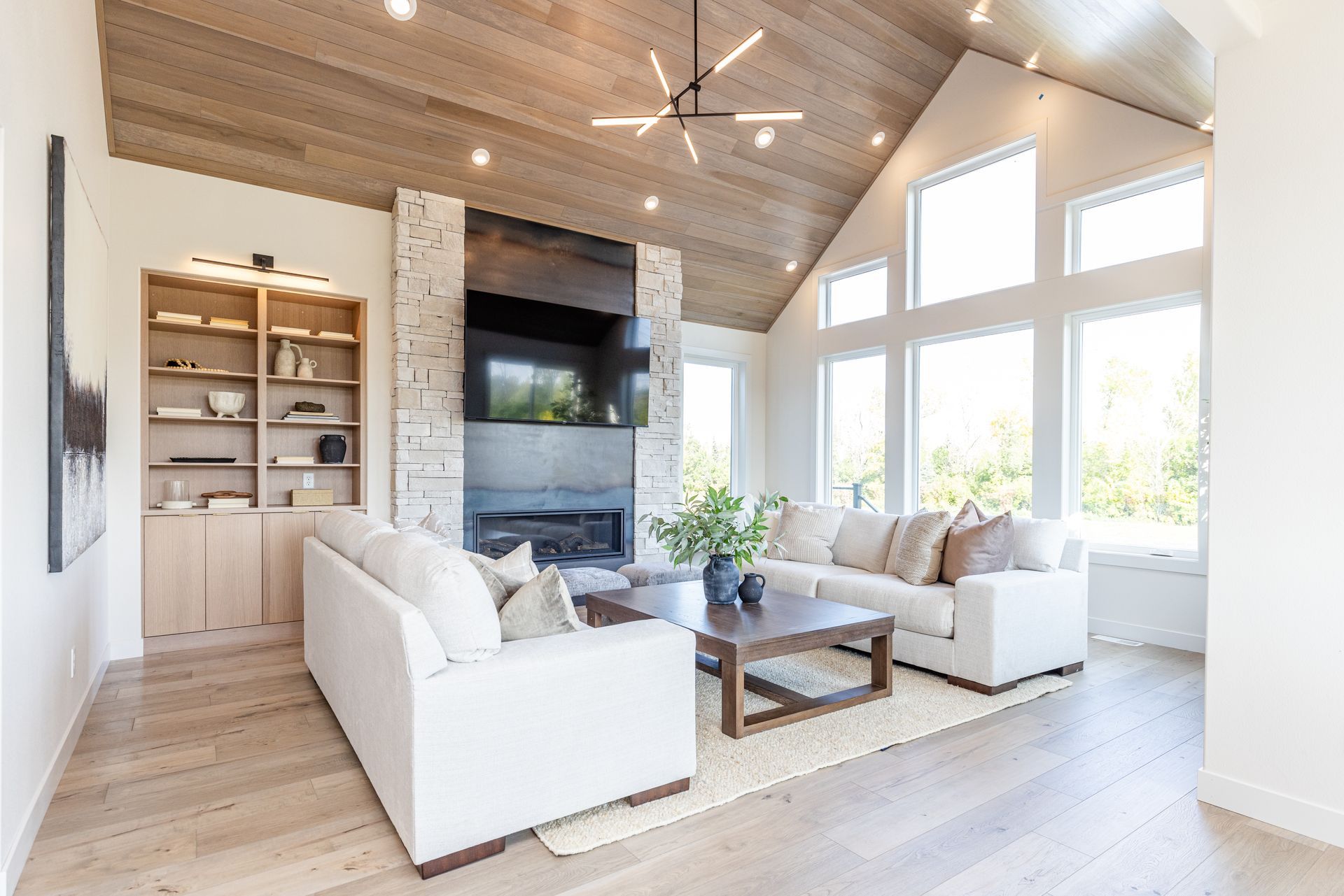 Living room with fireplace, white couches, and large windows. Light wood floors and ceiling.