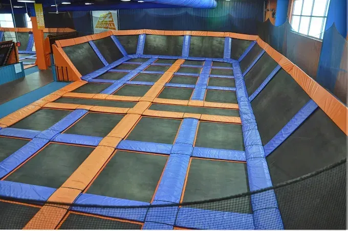 Sky Zone Trampoline Park Fargo ND An indoor trampoline park with a large jumping area, orange and blue padded borders, and angled side trampolines.