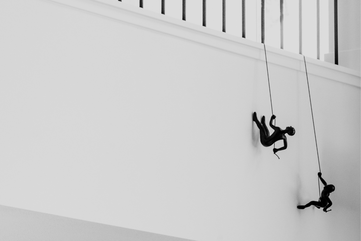 Two climbers hang from ropes on a white indoor wall