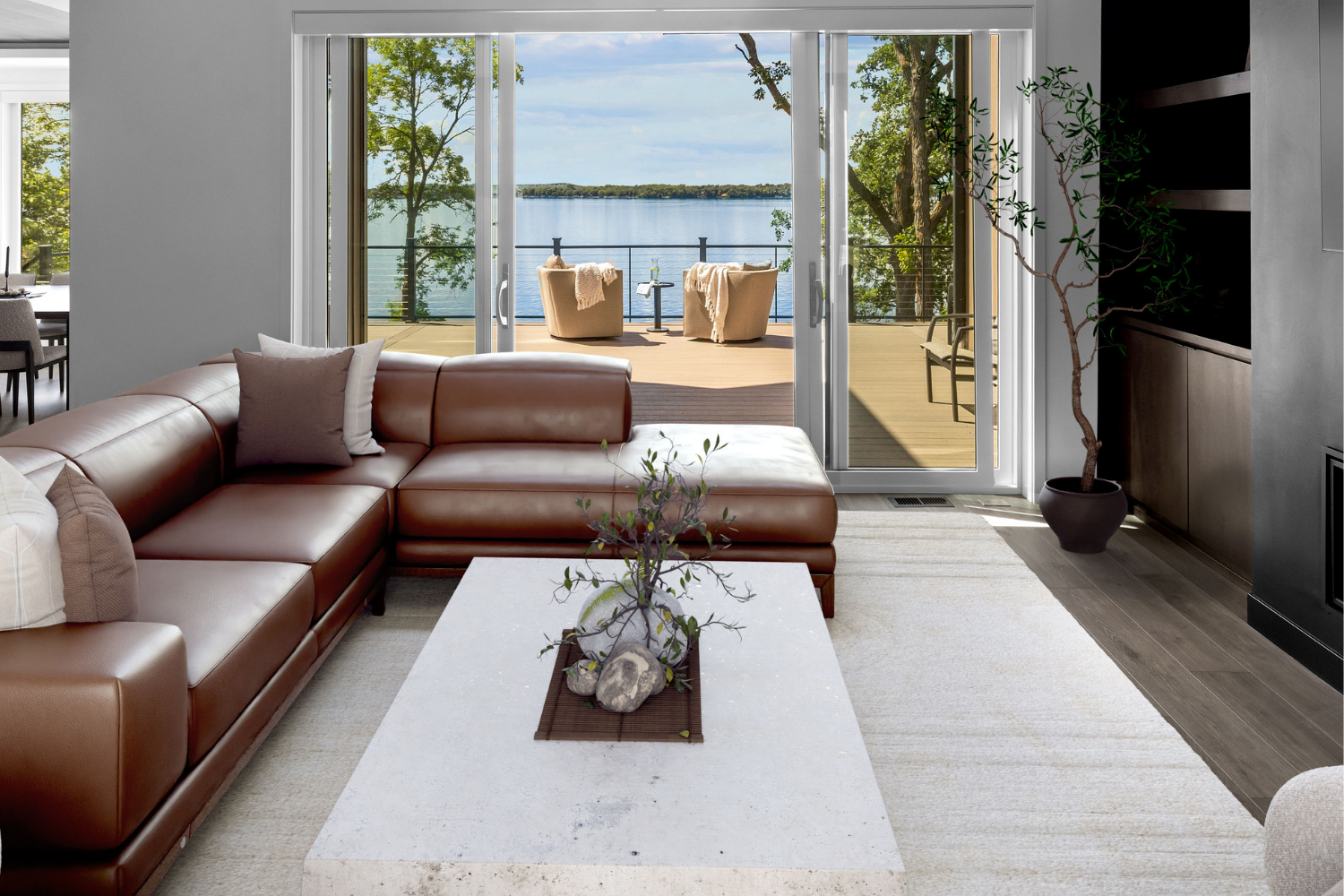 Modern living room with brown sectional, white rug, and sliding doors opening to a lake view
