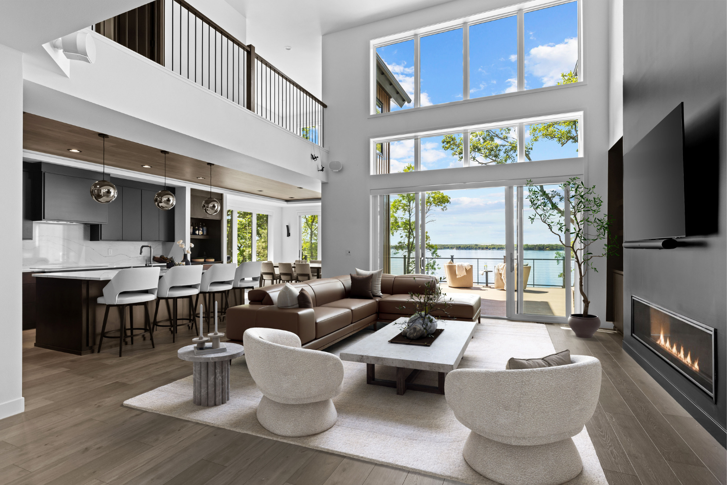 Modern open-plan living room with fireplace, lofted ceiling, large windows, and view of the water