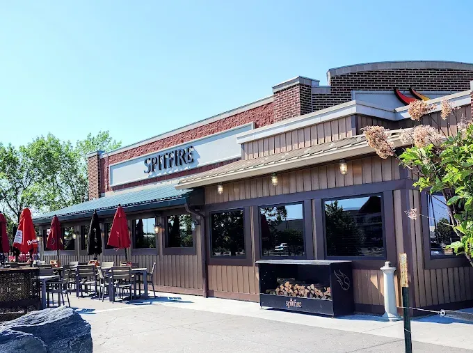 Spitfire Bar & Grill A Spitfire restaurant building with brown wooden siding, large windows, and outdoor patio tables under red umbrellas.