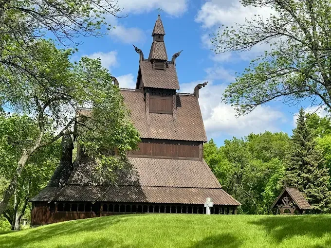The Hjemkomst Center The Hopperstad Stave Church replica features dark wood, layered roofs, and dragon head gables on a grassy hill under sky.