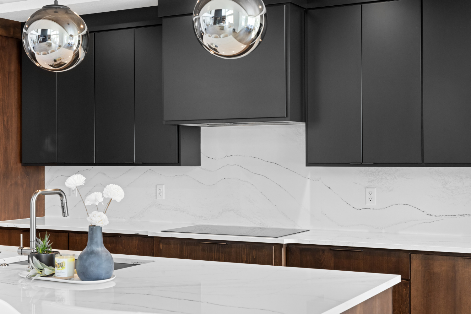 Modern kitchen with black cabinets, white marble backsplash, and white island under chrome pendant lights