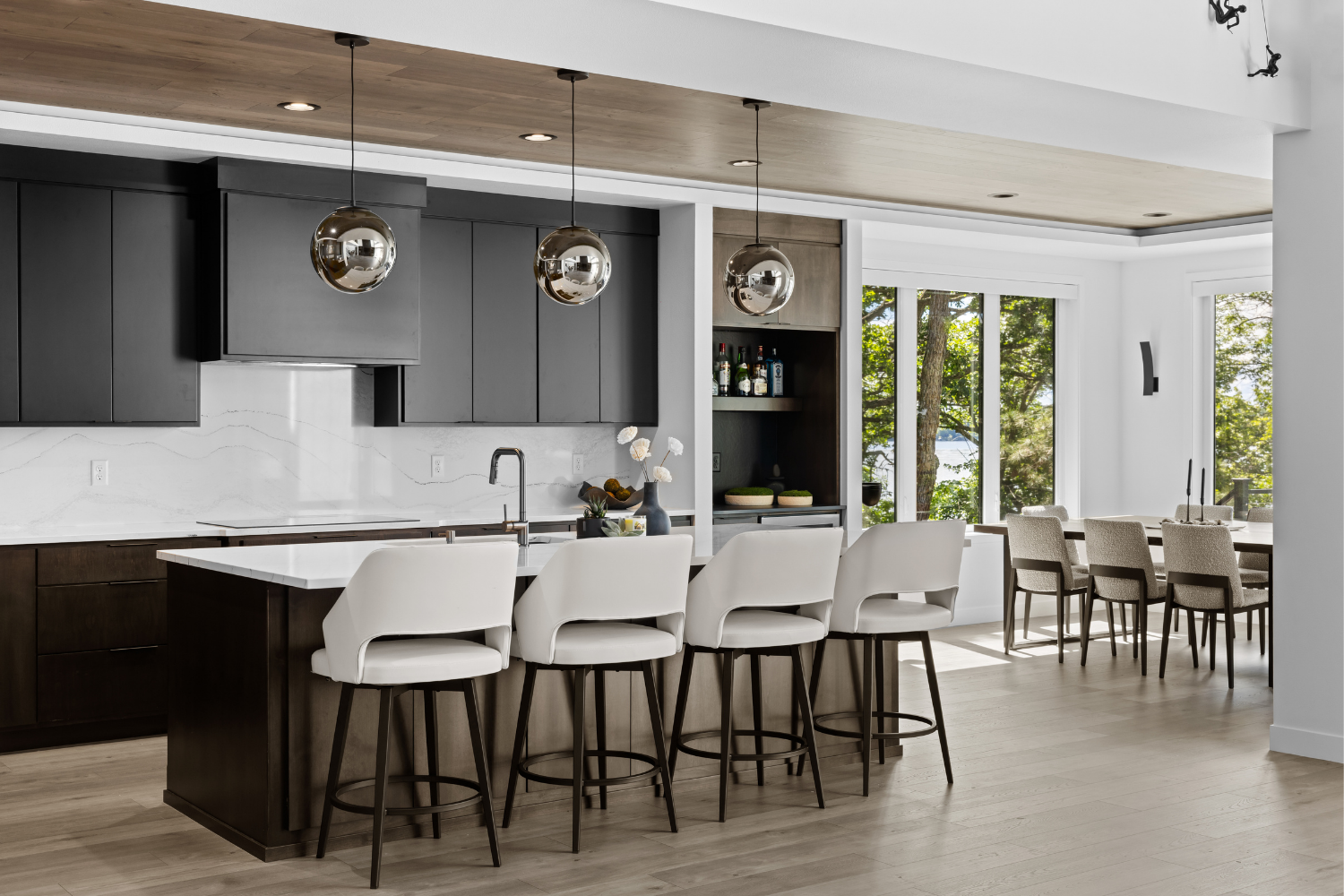 Modern kitchen with dark cabinets, white island, pendant lights, and stools beside a bright dining area