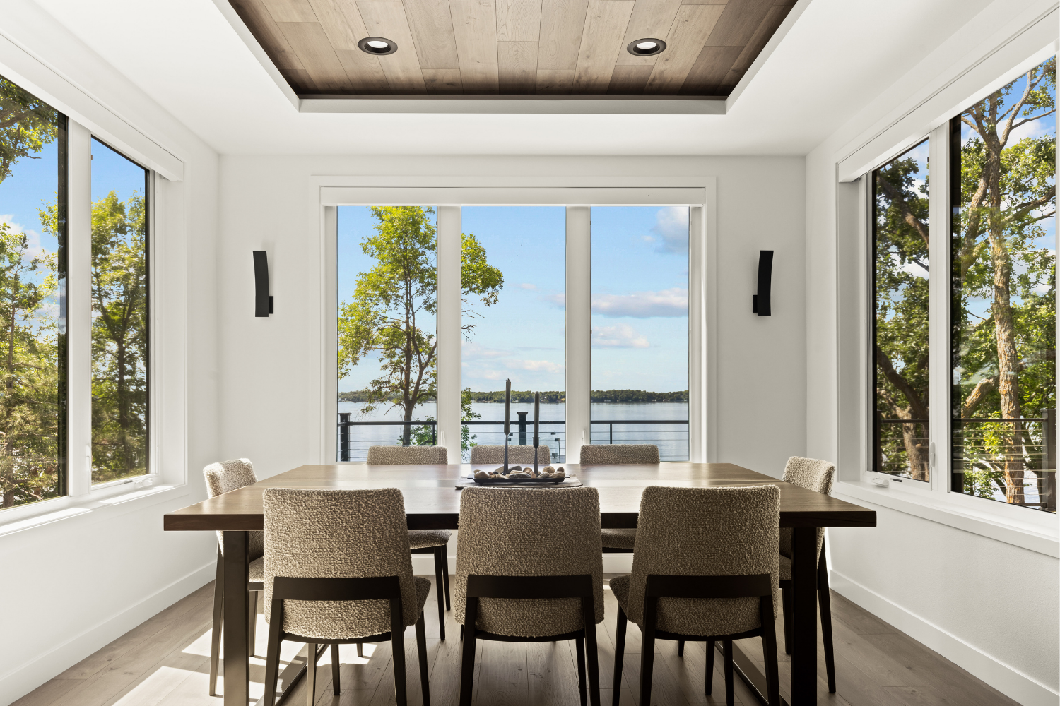 Bright dining room with four chairs, large windows, and a view of water and trees