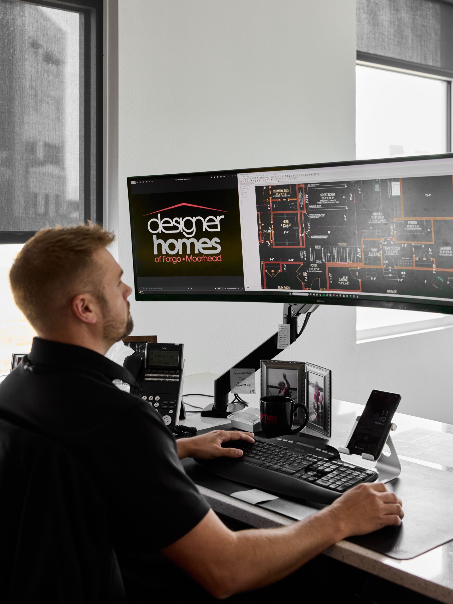 Person working at a desk with dual monitors showing home design plans in a modern office