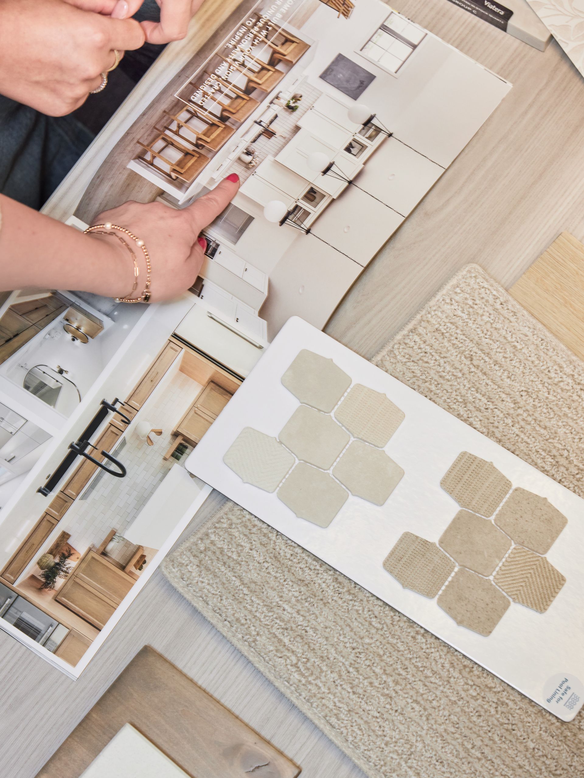 Hands pointing at interior design mood boards with beige fabric and room layout samples