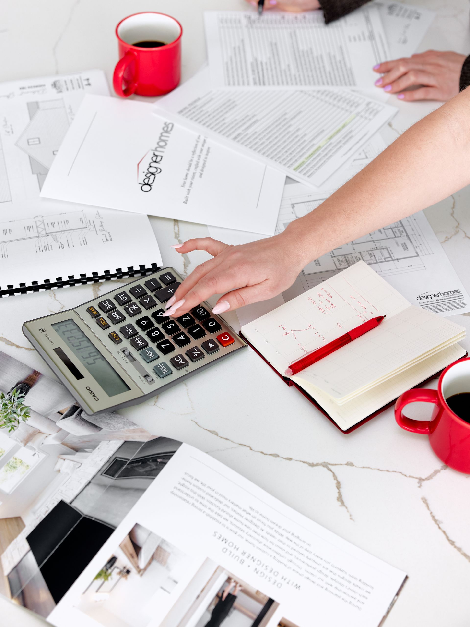 Calculator on a desk with scattered papers, red mugs, and a notebook during paperwork.