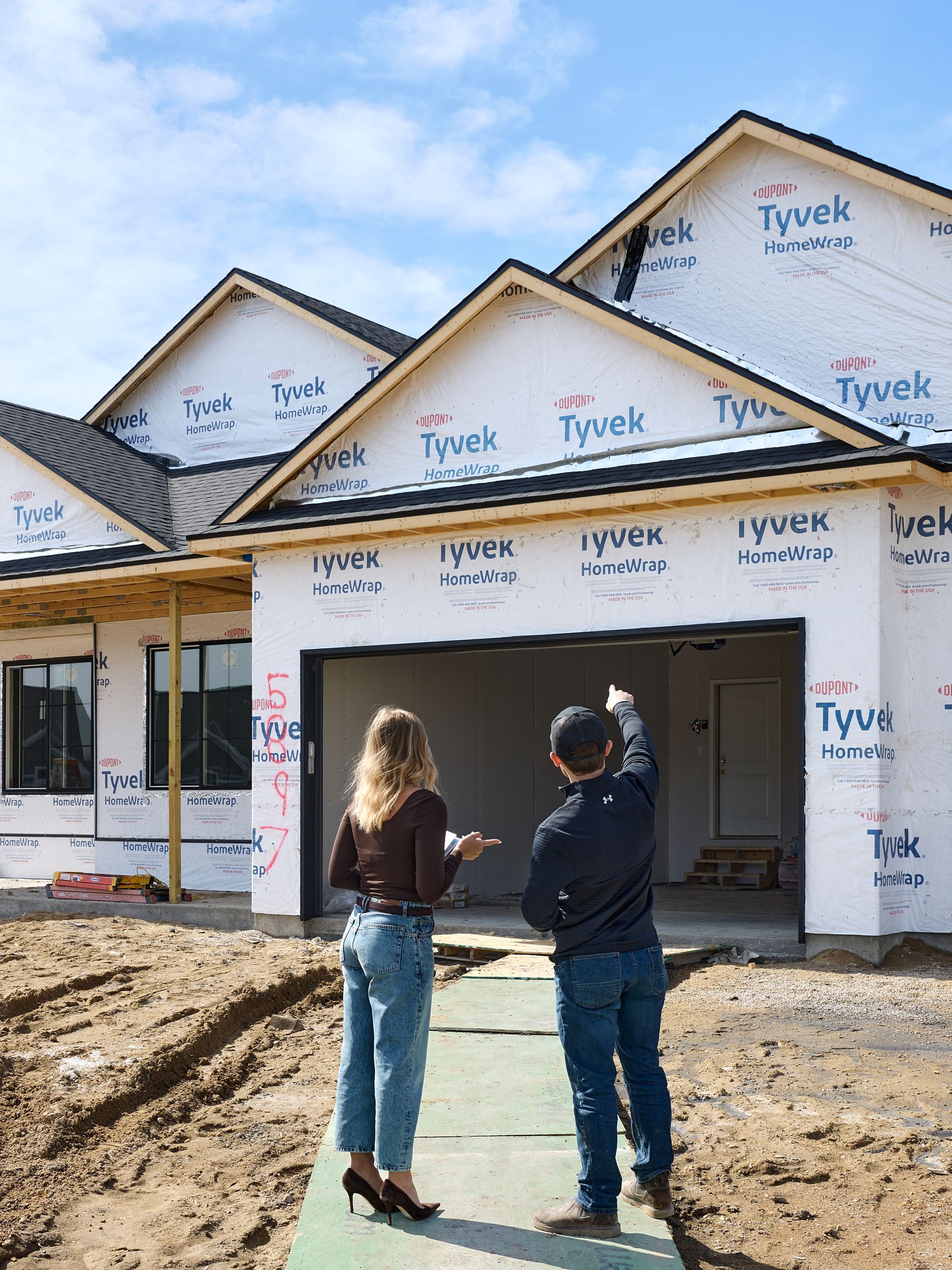 Two people stand outside a partially built house wrapped in Tyvek house wrap.
