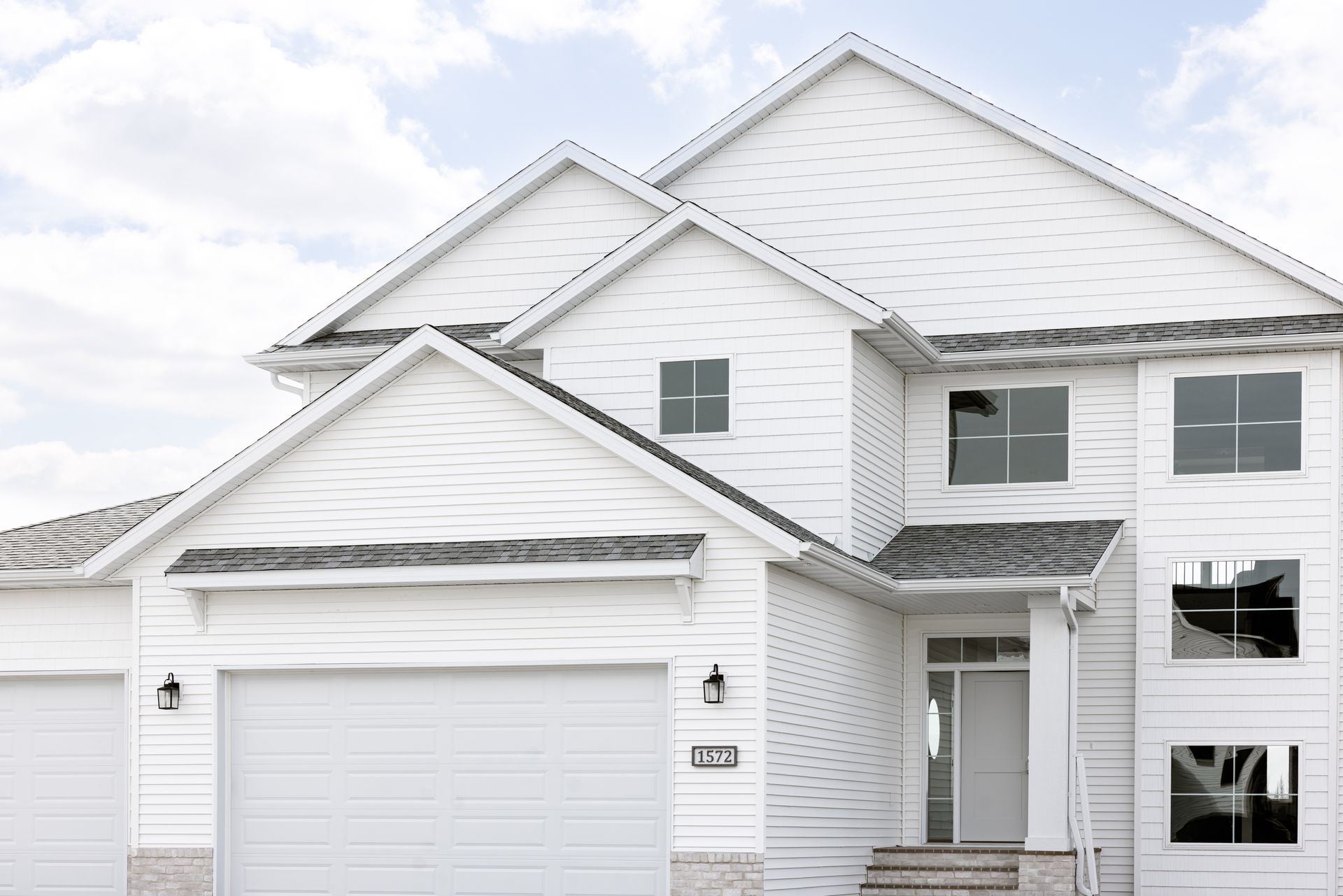 White two-story suburban house with attached garage and front porch under a cloudy sky