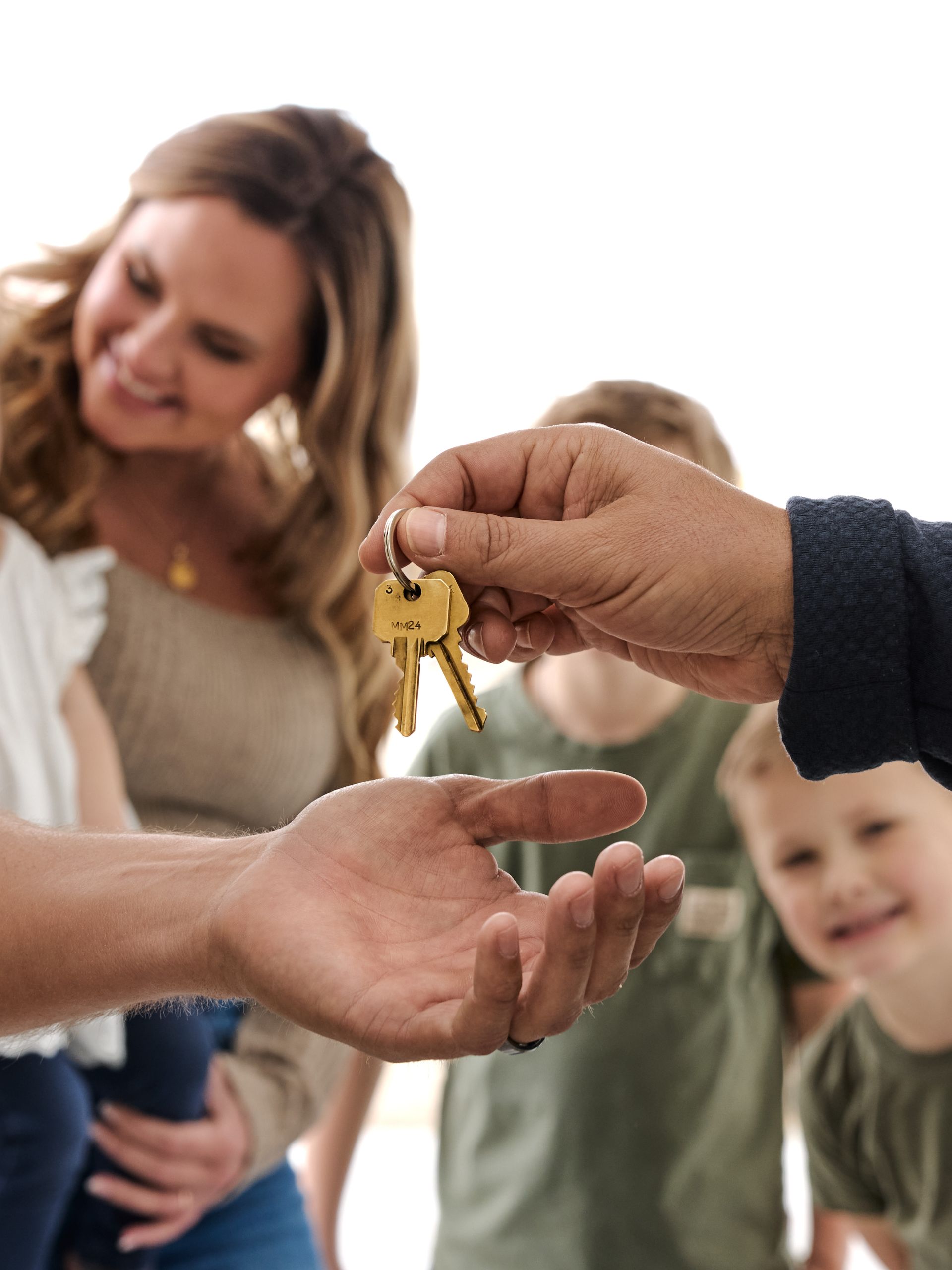 Handing over house keys to an outstretched hand, with a smiling family in the background