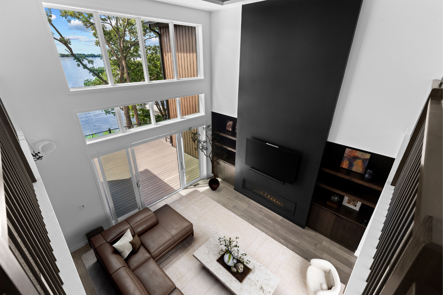 Modern living room with tall windows, brown sectional sofa, white rug, and a black accent wall with TV and shelves