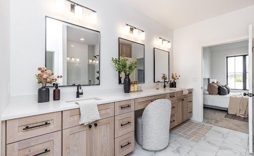 Pale wood cabinetry warms the white quartz, marble-look floor tile and crisp black fixtures in the primary bath.
