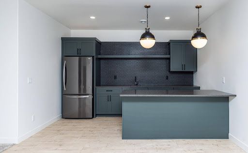 Deep blue-green cabinetry, black hex tile and warm metal accents give the lower-level bar its own confident mood.
