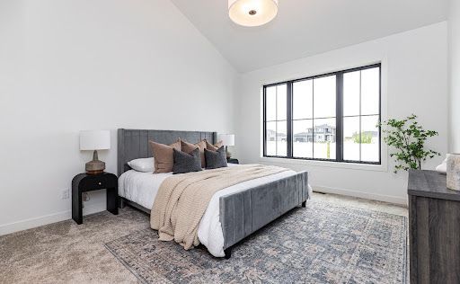 A vaulted ceiling and oversized black-framed window give the primary bedroom an airy, restful presence.
