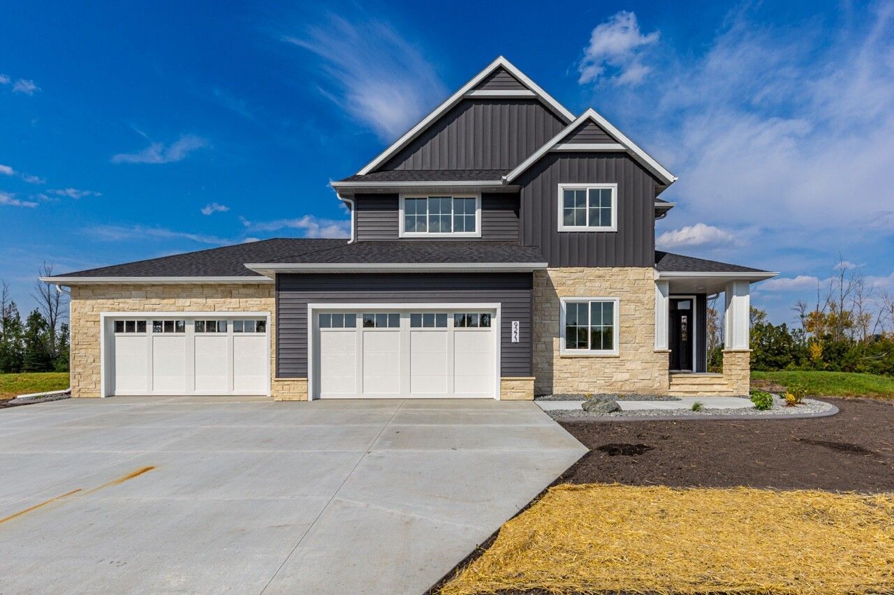 Modern two-story suburban house with gray siding, stone accents, and a three-car garage under a blue sky