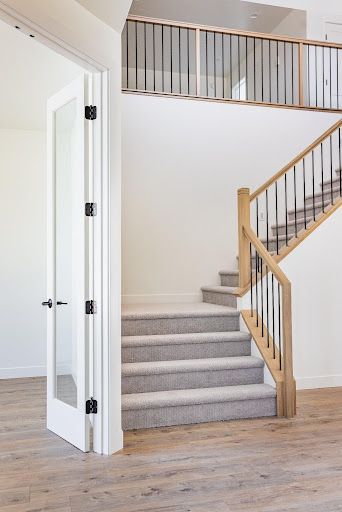 Interior staircase with light wood railing, gray carpeted steps, and white walls in a bright entryway