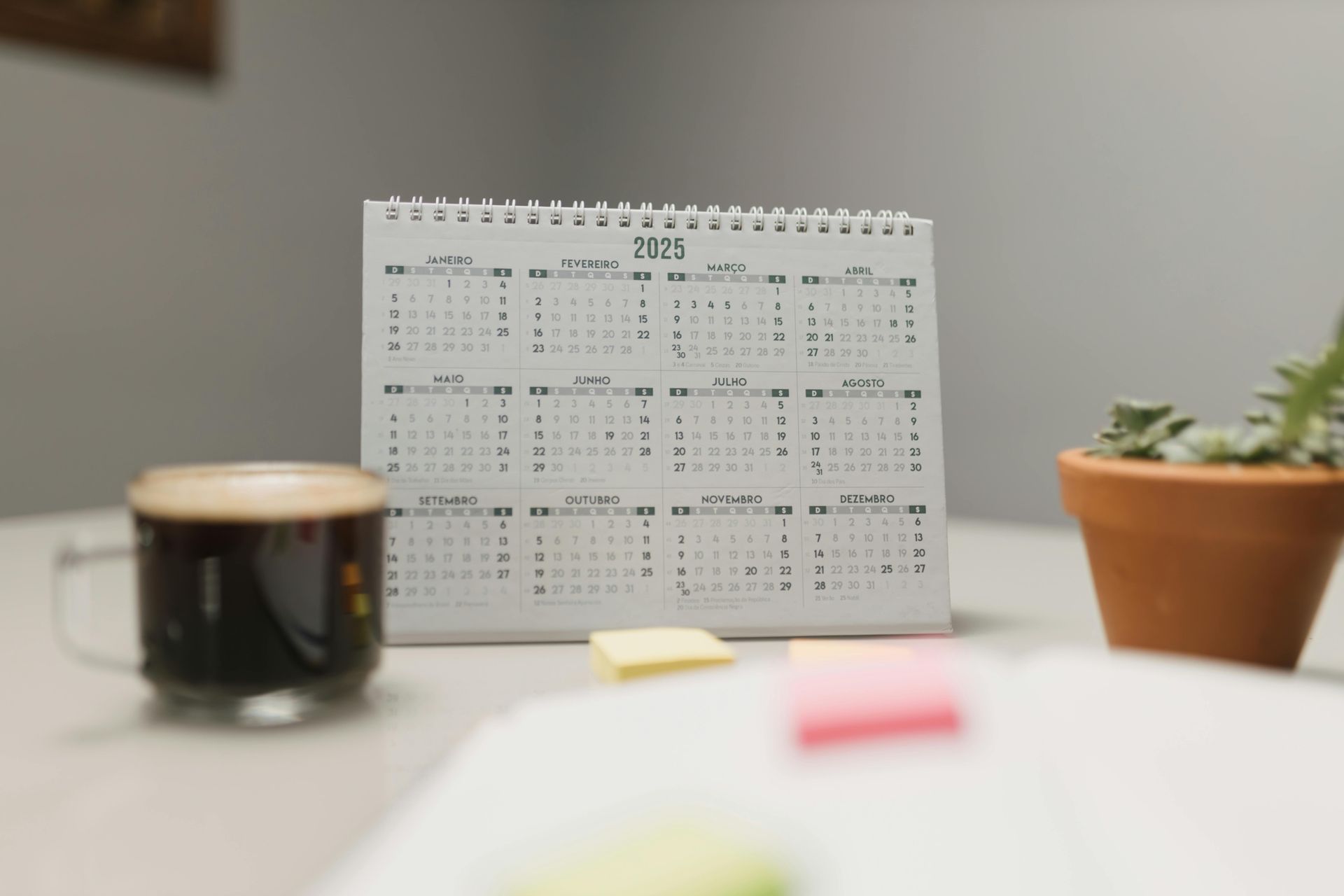 Desk with calendar, coffee, plant, and sticky notes.