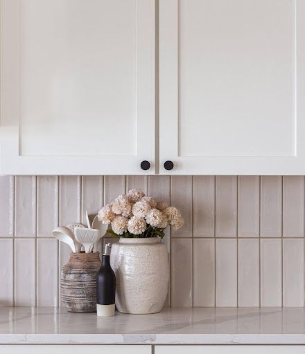 The palette depends on texture rather than color alone: softly reflective backsplash tile, handmade-looking ceramics, veined counters and fine vertical fluting at the fireplace.
