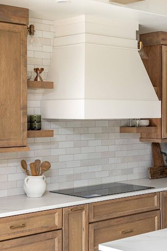 Modern kitchen with white range hood, wood cabinets, and gray tile backsplash
