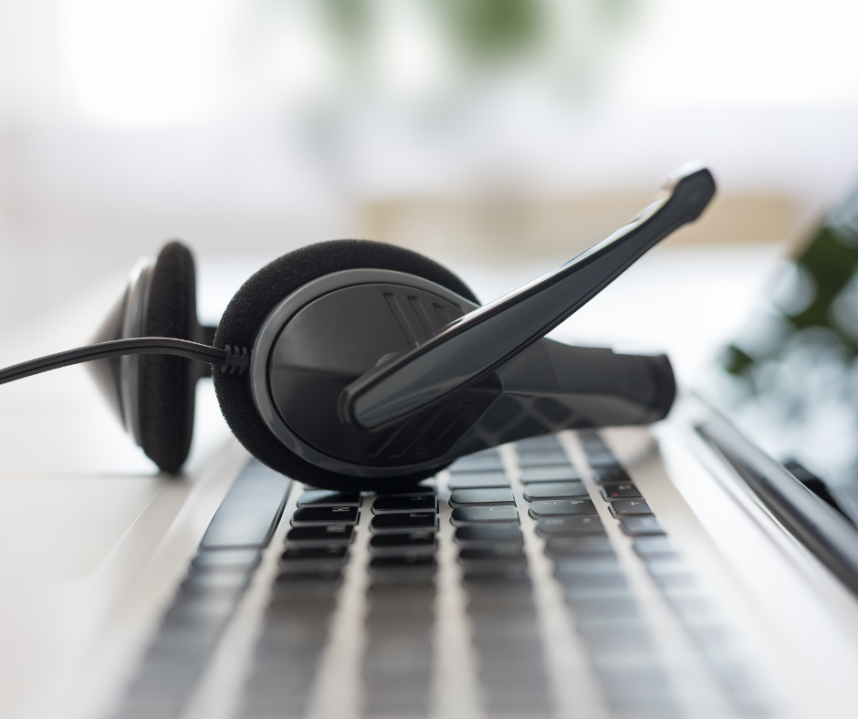 Headset resting on a laptop keyboard. Black headset, white laptop, blurred background.