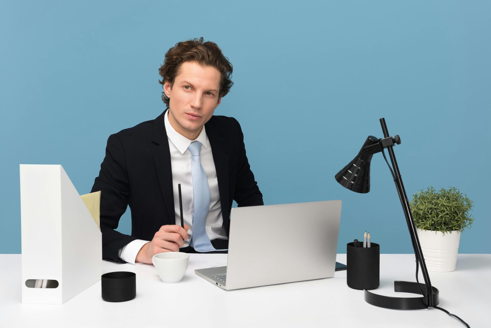 A man in a suit and tie is sitting at a desk with a laptop.
