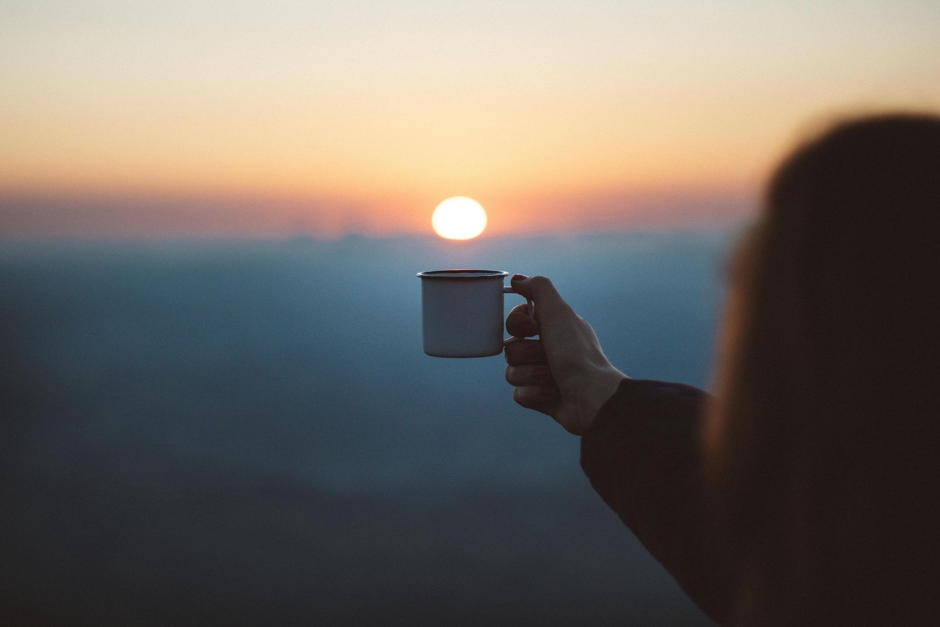 Hand holding a mug at sunrise, with a blurred horizon in the background
